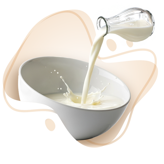 Glass pitcher pouring milk into a white bowl with a beige background